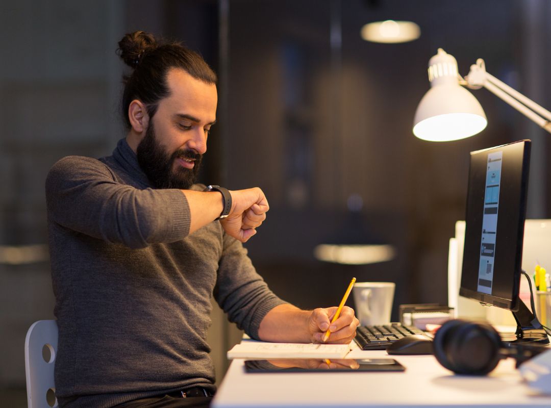 Person sitzt am Schreibtisch und schaut auf seine Smartwatch. Smartwatch Band.